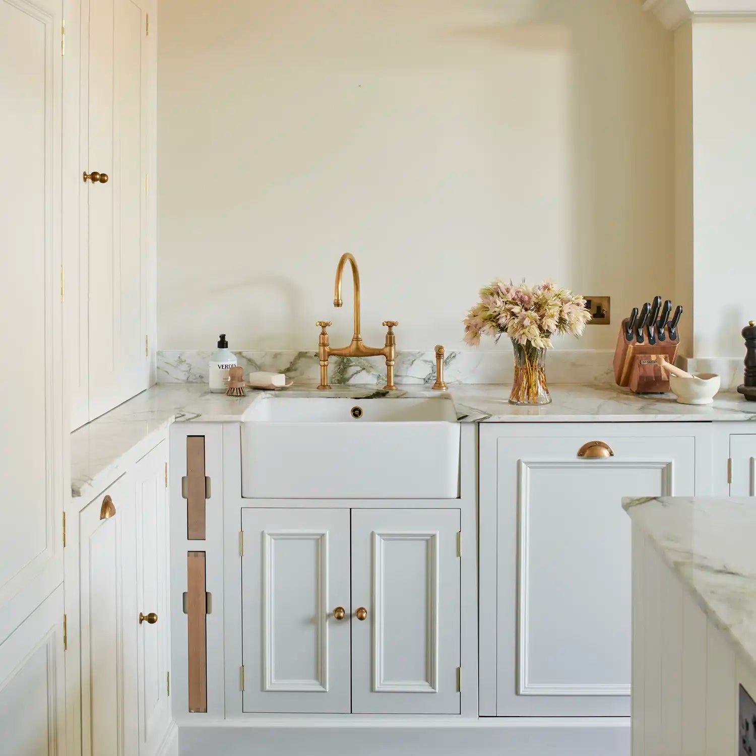 Shell white painted Chichester kitchen with marble worktops, farmhouse sink, integrated chopping boards and aged brass tap and brass  cup handles.