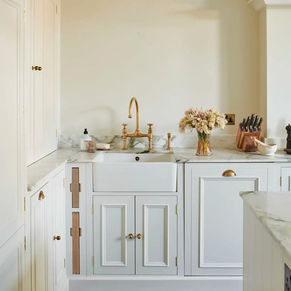Shell white painted Chichester kitchen with marble worktops, farmhouse sink, integrated chopping boards and aged brass tap and brass  cup handles.