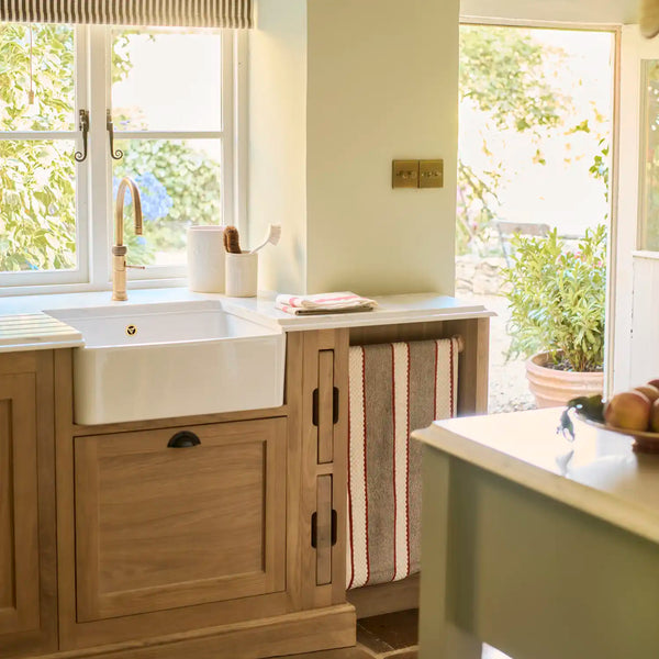 Henley oak sink cabinet with farmhouse sink, brass tap and garden view.