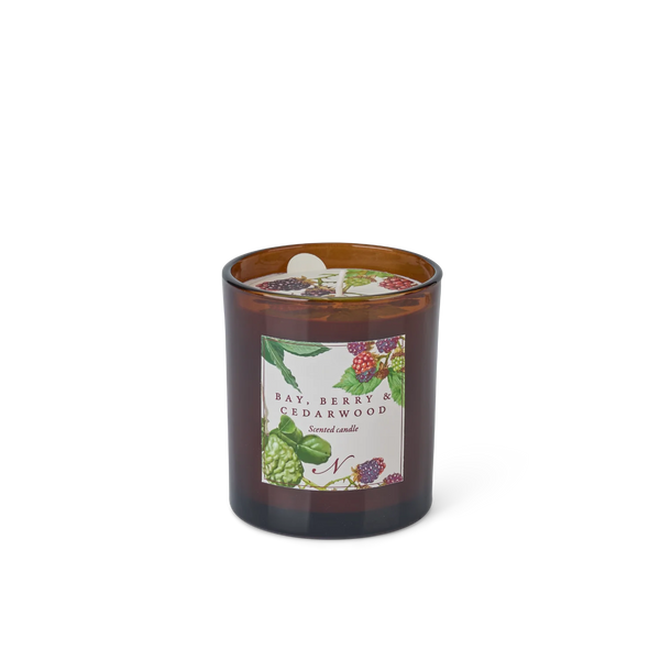 An amber glass jar candle with a white label featuring berry and citrus botanical illustrations, reading 'Bay, Berry & Cedarwood Scented Candle'.