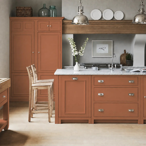 Chichester kitchen with cabinetry painted in Burnt Sienna terracotta orange, featuring a central island and oak bar stools.