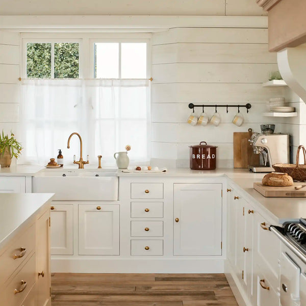 Henley kitchen painted in white Snow with farmhouse sink, brass hardware , neutral cream Polenta island and warm wooden flooring.