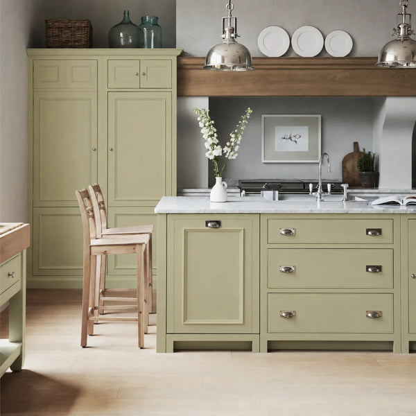 Chichester kitchen with cabinetry painted in Quince green, featuring a central island and oak bar stools.