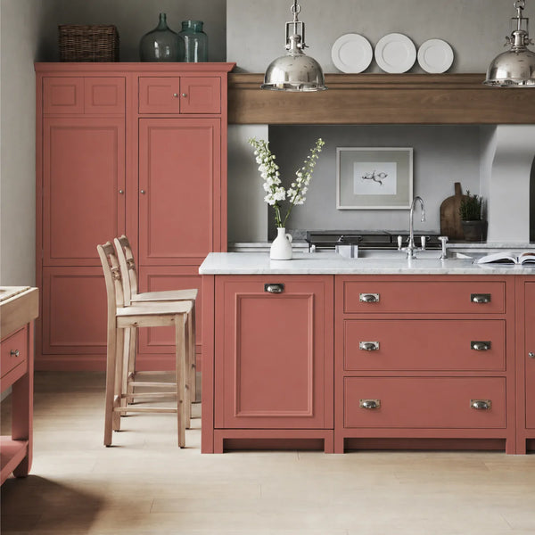 Chichester kitchen with cabinetry painted in Rhubarb red pink, featuring a central island and oak bar stools.