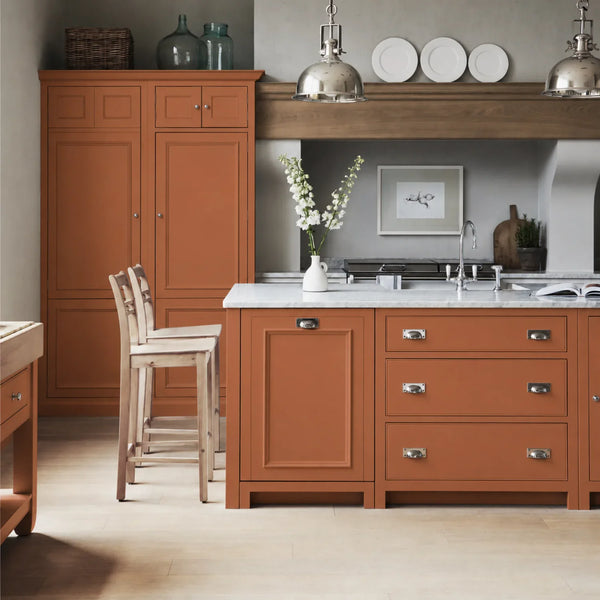 Chichester kitchen with cabinetry painted in Bracken burnt orange, featuring a central island and oak bar stools.