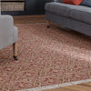 A rectangular area rug with a distressed geometric pattern in dusty rose and beige, styled in a living room setting on a wooden floor between gray sofas.