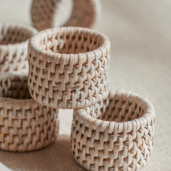 A close-up of several woven natural-fibre cylindrical napkin rings stacked together on a neutral fabric surface.