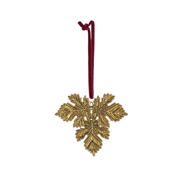 A gold-toned metal snowflake ornament with a textured leaf design, hanging from a dark red cord on a plain white background.