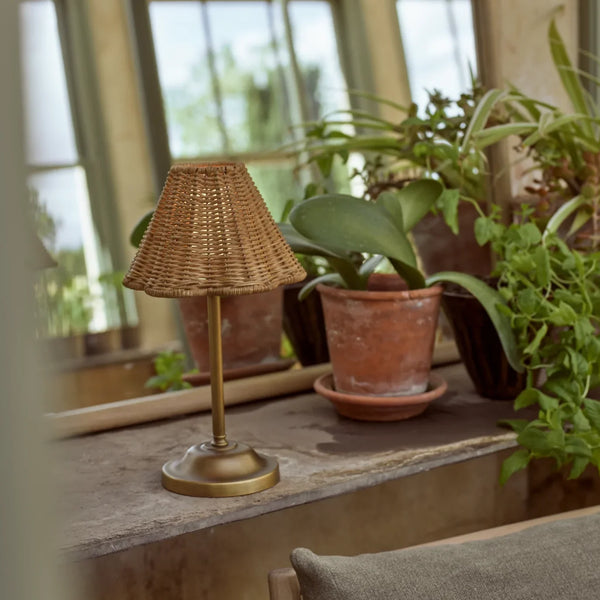 Athena Portable brass and rattan table lamp in garden room next to mirror and plants in terracotta pots