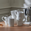 A set of white ceramic mugs with a ribbed texture and curved handles, arranged on a wooden table next to a silver moka pot.