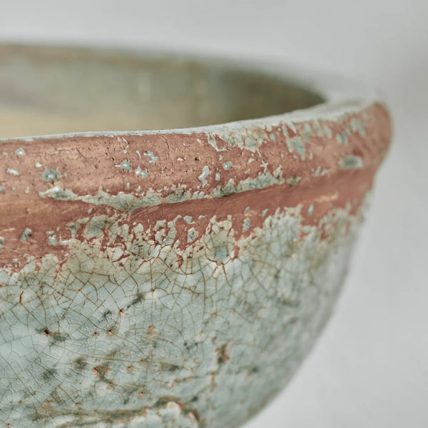 Close-up of a ceramic bowl showing a textured, crackled glaze in pale sage green and a terracotta-colored band around the rim.