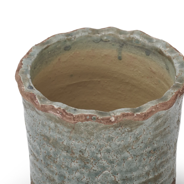 Close-up of a handmade ceramic planter with a scalloped rim, featuring a textured glaze in muted blue-green with brown earthy undertones and a warm beige interior.