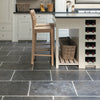 A modern kitchen interior with dark slate tile flooring, white cabinetry, a light wood bar stool, a wicker basket, and a built-in wine rack on the island.