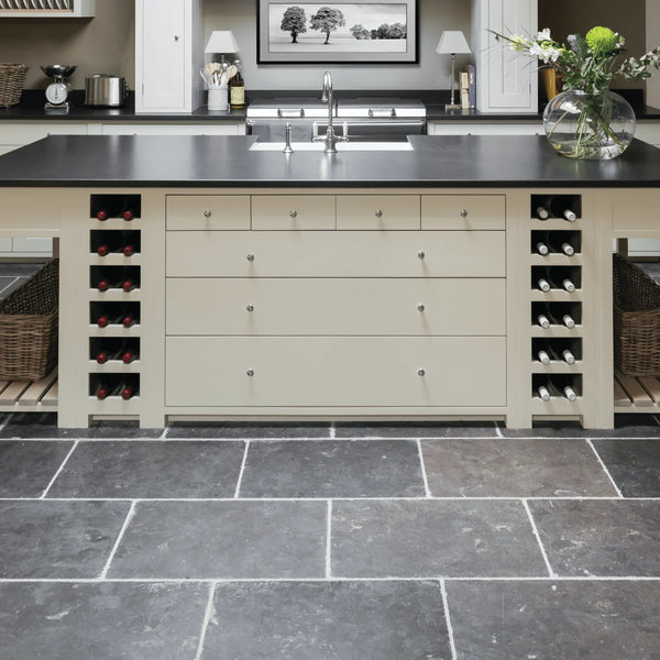 A cream-colored kitchen island with a black countertop, featuring multiple drawers, wine bottle storage compartments on both sides, and a double sink, set against a modern kitchen background with dark slate tile flooring.