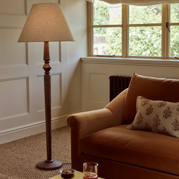 Chalford darkened oak floor lamp in upscale living room with caramel boucle sofa, woven carpet and cream paneled walls