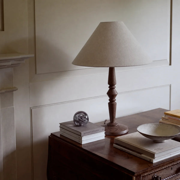 Chalford Darkened Oak Table Lamp with Linen tapered lamp shade on side table with coffee table books and ornaments