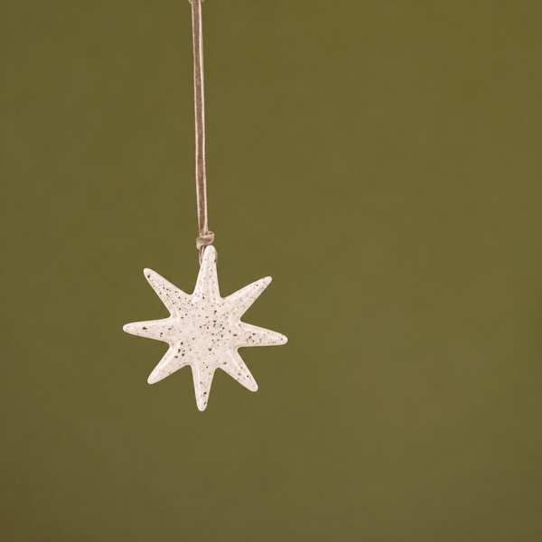 A small white ceramic star-shaped ornament with subtle red speckles, hanging from a thin string against a solid olive green background.