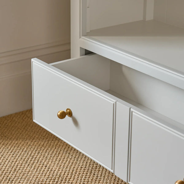 A close-up of a white wooden drawer with a brass round knob, shown partially open on a woven jute rug.