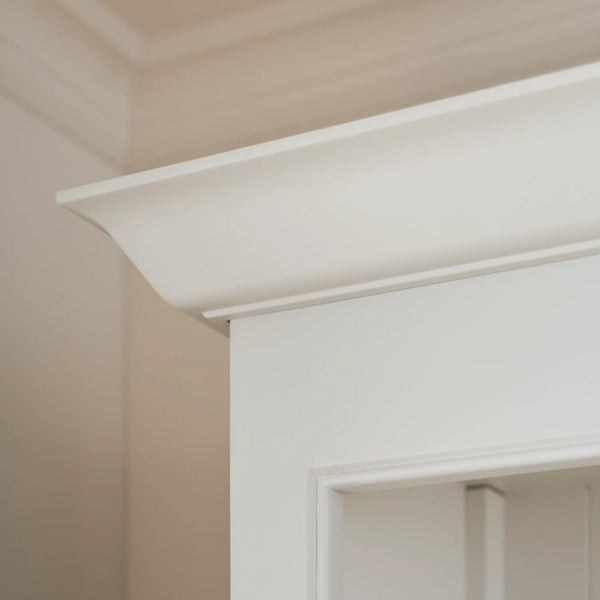 Close-up of a white decorative architectural shelf trim against a warm beige wall and ceiling.