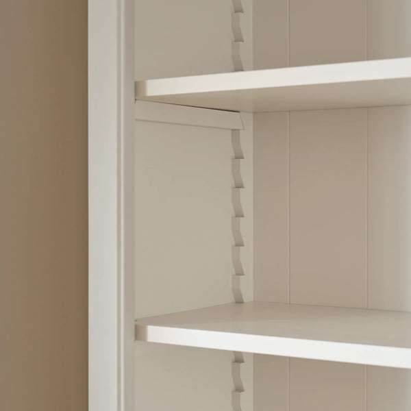 Close-up of a white adjustable shelving unit with wavy tension rods and a beige wall on the left.