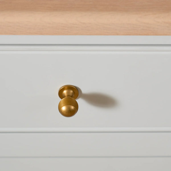 A close-up of a brass drawer knob mounted on a white paneled cabinet, with a light wood surface visible at the top.