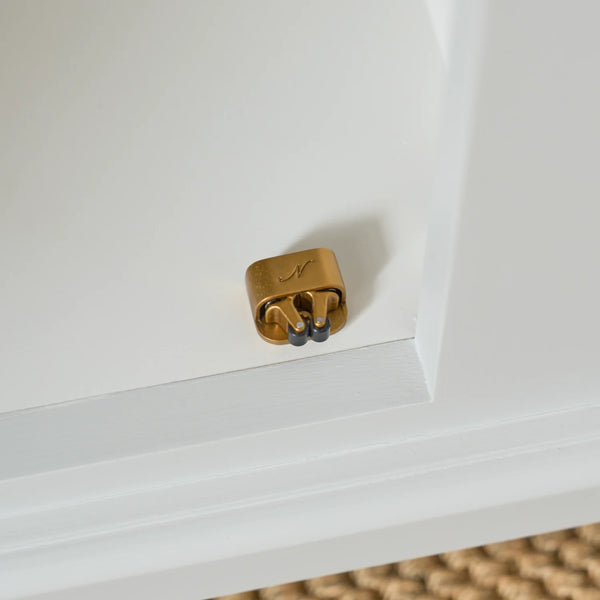 A small brass door stopper with two dark rubber pads, mounted on the edge of a white wooden cabinet door.