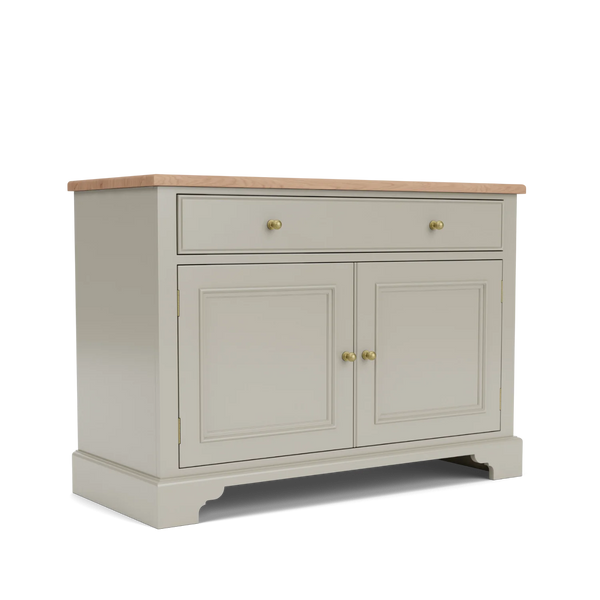 A classic sideboard cabinet with a light beige painted finish, a natural oak wood top, two drawers at the top with brass knobs, and two paneled doors below with matching knobs, shown on a white background.