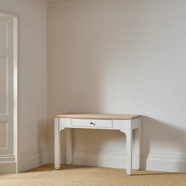 A small white console table with a light natural wood top and a single drawer, set against a neutral cream-colored wall and beige carpet.