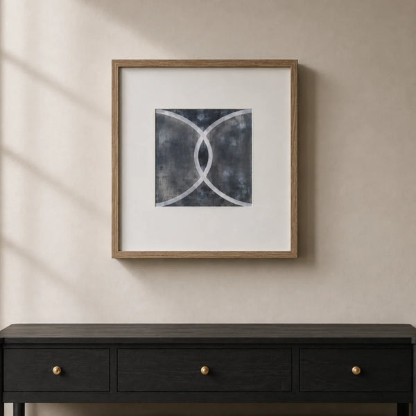 Framed abstract wall art hanging above a dark console table against a warm beige wall, with soft window shadows cast across the scene.