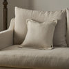 A light beige textured throw pillow resting on a matching beige upholstered armchair, with a larger matching back cushion behind it.