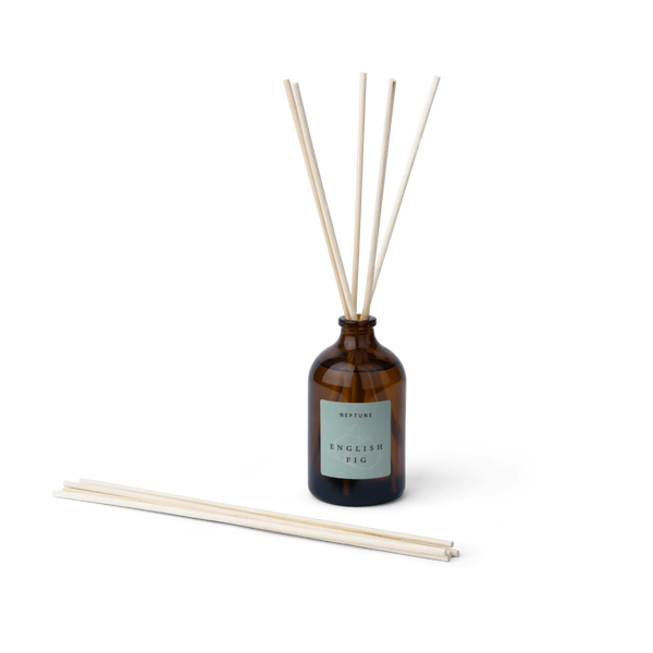 Amber glass reed diffuser bottle with a pale green label reading 'NEPTUNE ENGLISH FIG', shown with four reeds standing up and two additional reeds lying on the surface against a white background.