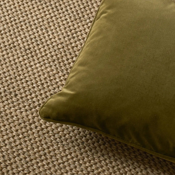 An olive green velvet throw pillow resting on a textured beige woven rug.