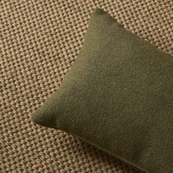 An olive green rectangular throw pillow with a textured fabric cover, resting on a woven beige rug.