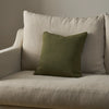 An olive green textured throw pillow resting on a light beige upholstered armchair against a neutral gray wall.