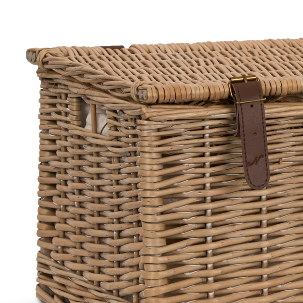 Close-up of a woven wicker storage basket or trunk with a hinged lid and a brown leather strap closure on a white background.