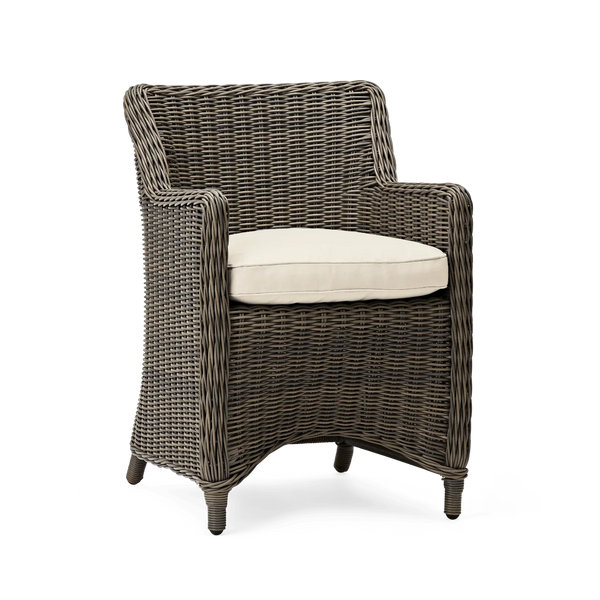 A wicker armchair with a dark brown woven frame and a light beige seat cushion, shown against a plain white background.