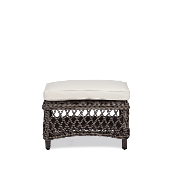 A dark brown wicker ottoman with a thick, square off-white cushion on top, shown against a plain white background.