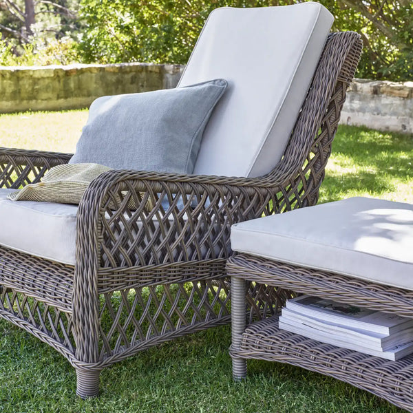 Gray wicker outdoor patio furniture set with a lounge chair and matching ottoman, featuring light gray and beige cushions on a grassy lawn.