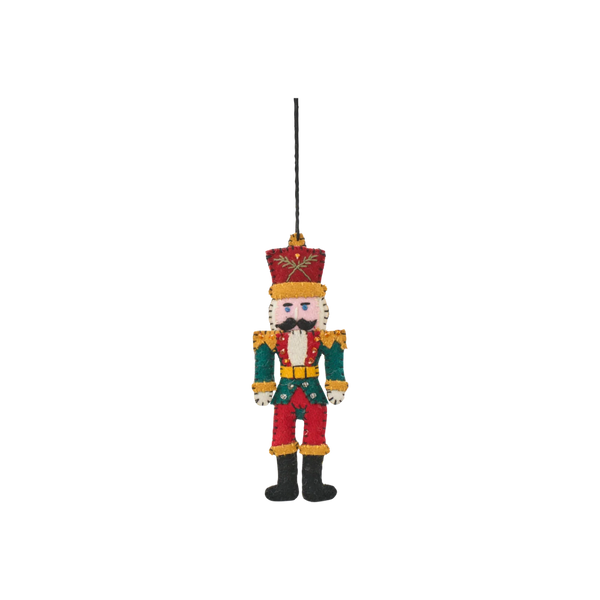 A small nutcracker figurine hanging from a black string, featuring a red and green uniform, gold trim, a red hat, black boots, and a white face on a plain white background.