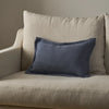 A rectangular navy blue throw pillow with a subtle woven texture, styled on a light beige linen armchair against a neutral beige wall.