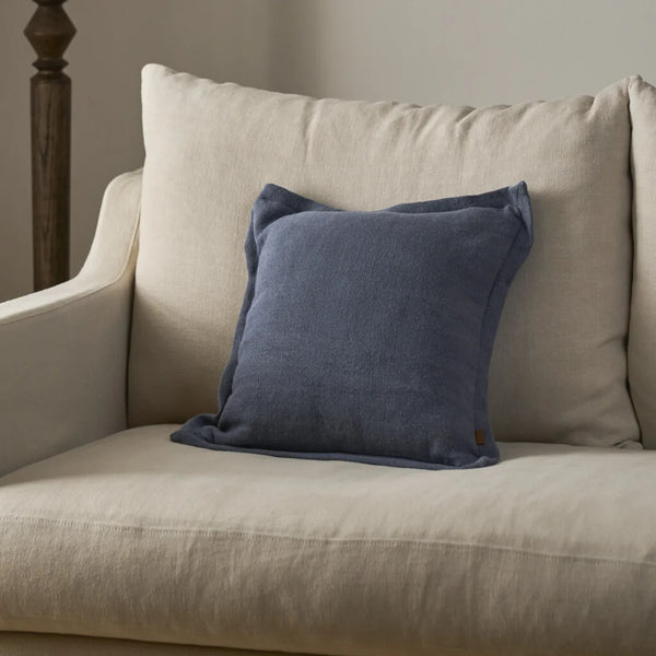 A navy blue textured throw pillow resting on a light beige linen armchair in a softly lit room.