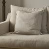 A light beige textured throw pillow resting on a matching beige upholstered armchair in a softly lit interior setting.