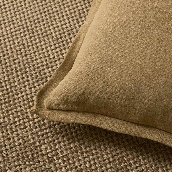 A close-up of a saffron yellow linen cushion resting on a textured brown woven rug.
