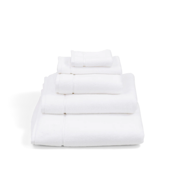A stack of five folded white cotton towels, including a bath towel, hand towel, and washcloths, arranged neatly on a white background.