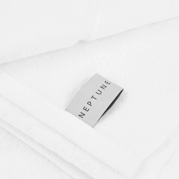 A close-up of folded white terry cloth towels with a small silver fabric tag printed with the brand name NEPTUNE.