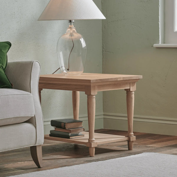 Wooden side table with a lamp and books next to a sofa in a living room.