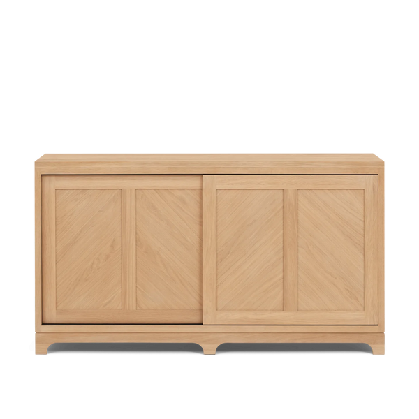 A light natural oak wood sideboard cabinet with two sliding doors featuring a chevron panel design, shown against a plain white background.