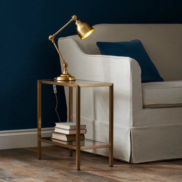 Gold lamp on a side table next to a beige sofa with blue cushions against a dark blue wall.