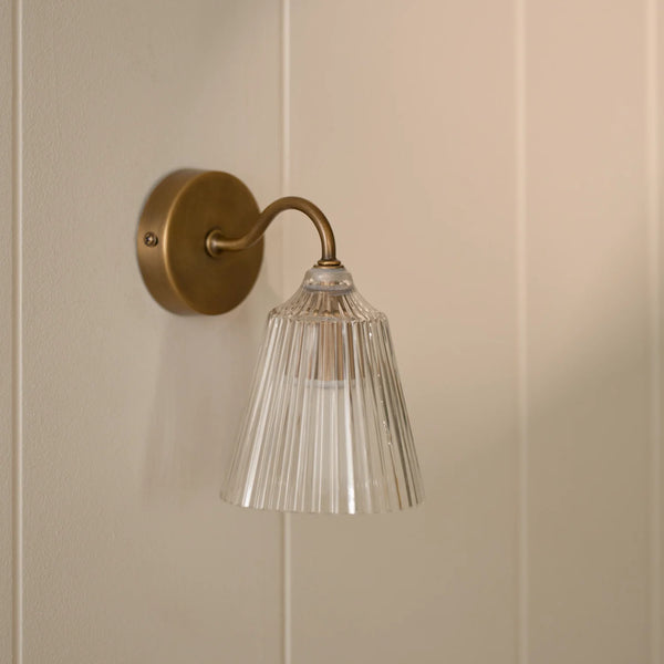 Lennox wall light with brushed brass base and glass shade on wall.
