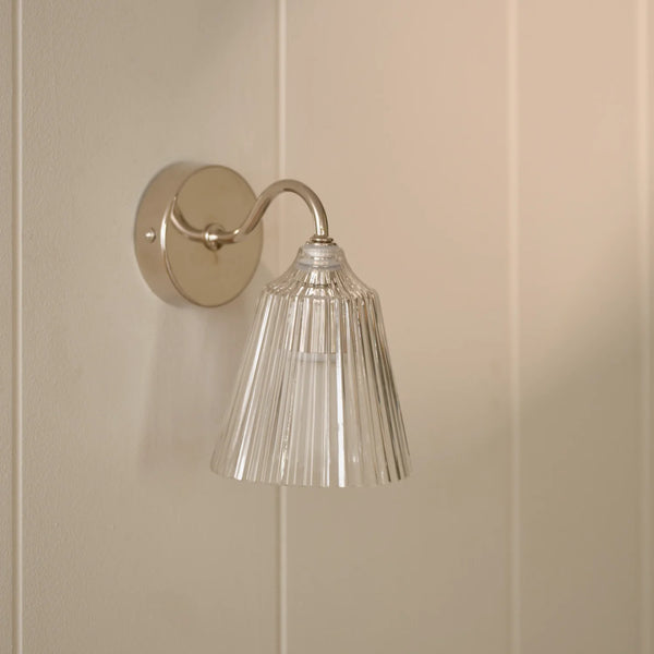 Lennox wall light with brushed nickel base and glass shade on wall.